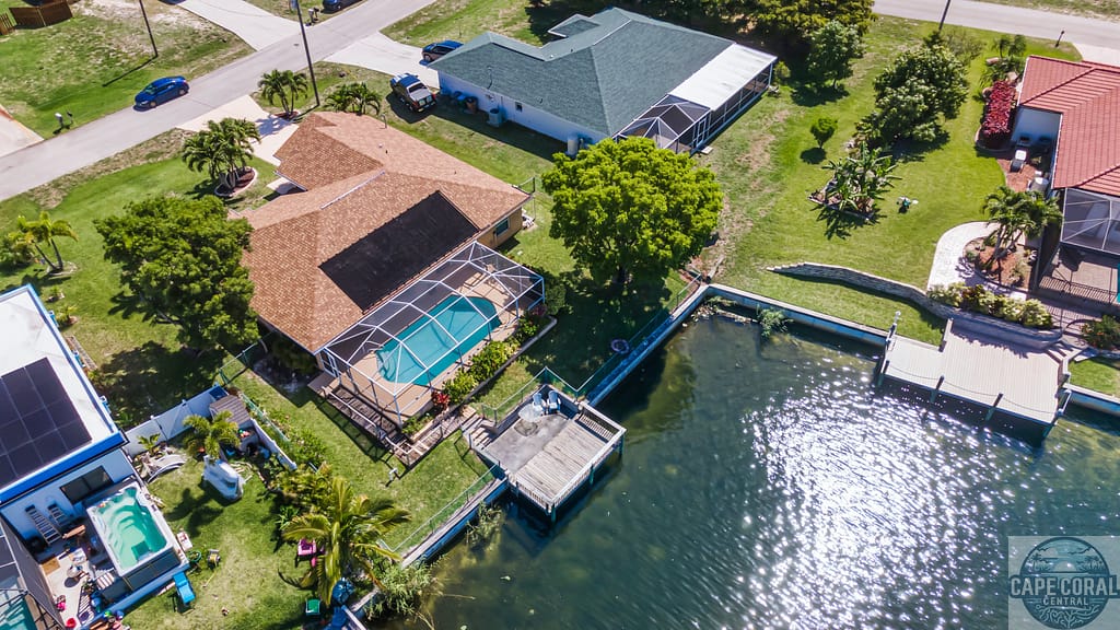 A bird's-eye view of a Cape Coral home with sailboat access, showcasing a private dock, pool, and verdant surroundings, epitomizing the quintessential Floridian waterfront living experience.