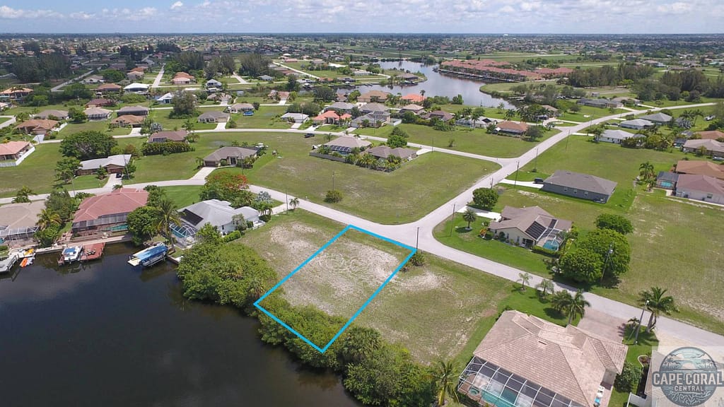 Aerial view of a vacant waterfront lot outlined in blue, located in North Cape Coral, Florida, amidst residential homes with canal access.