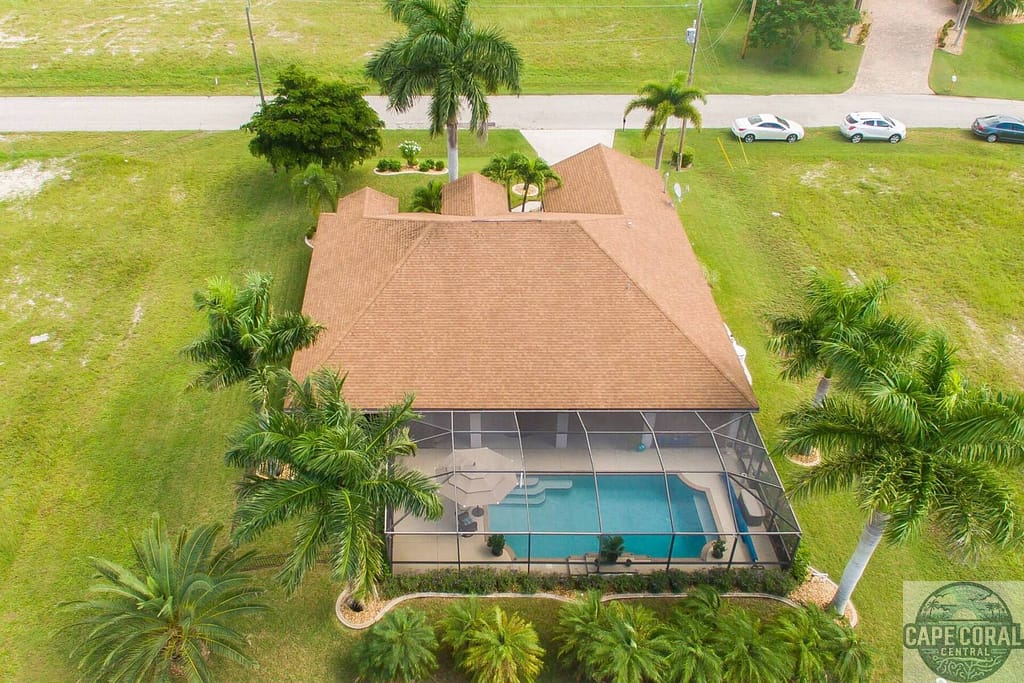 Aerial view of a large Alva property with a shingle roof and screened-in pool, surrounded by lush palm trees and well-kept lawns, symbolizing serene Florida living.