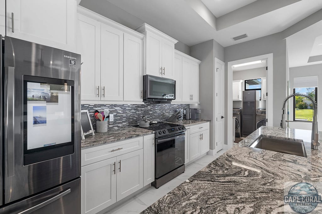 Contemporary Cape Coral kitchen in a new luxury home, with stainless steel appliances, white cabinets, and granite island, reflecting upscale modern living.