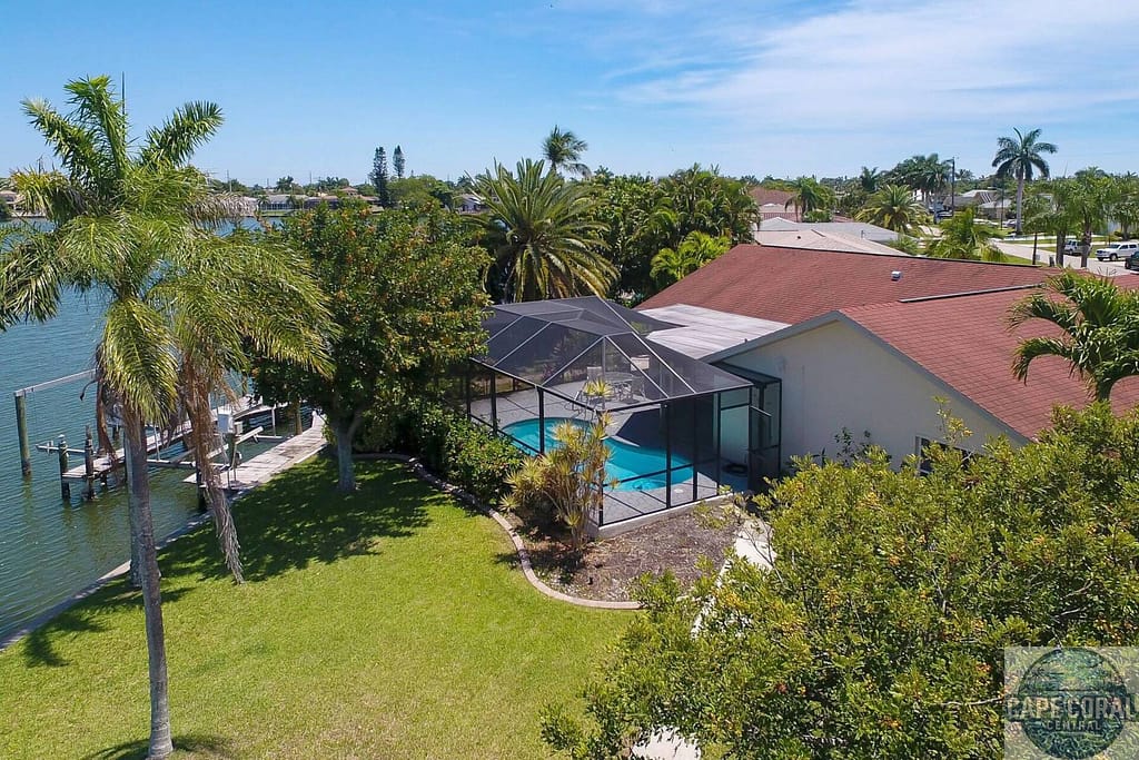 Aerial view of a Cape Coral home with sailboat access, featuring a private dock, swimming pool, and lush tropical landscaping, encapsulating the essence of Florida's waterfront lifestyle.