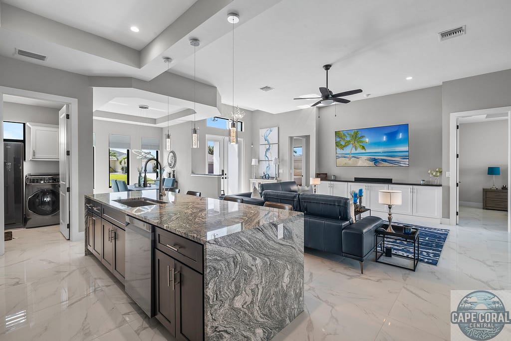 Elegant open-concept living area in a Captiva luxury waterfront home, featuring a large granite kitchen island, marble floors, and upscale decor with a panoramic beach-themed wall art.