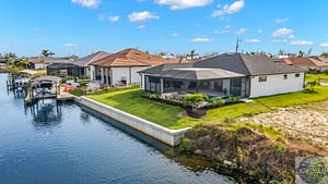 Waterfront properties in Cape Coral, FL, with a white modern home featuring a screened lanai, a lush green lawn, and a private boat dock