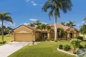 Single-family home in Fort Myers with a beige exterior, red trim, garage, and tropical landscaping including a prominent palm tree.