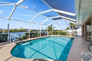 Screened pool patio with outdoor dining set, overlooking a peaceful canal in Cape Coral, Florida, under a bright blue sky.
